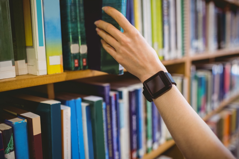 Student picking book in library wearing smart watch at the university